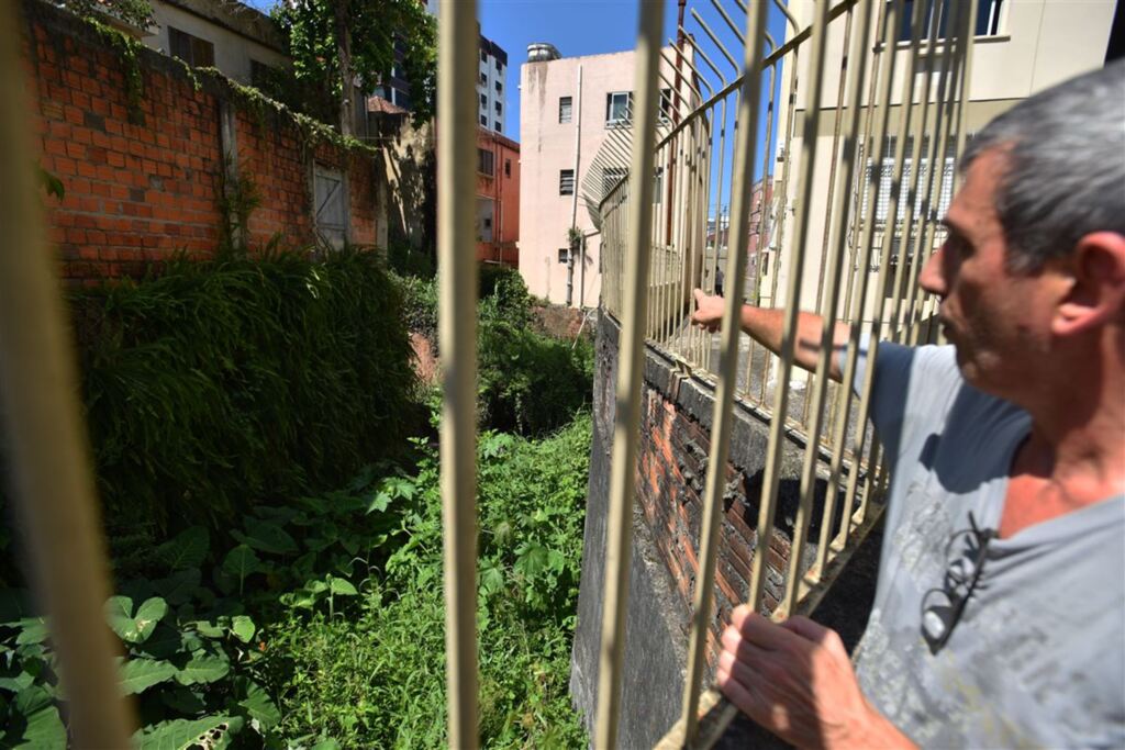Fotos: Gabriel Haesbaert (Diário) - O síndico Paulo Roberto Bastos mostra a situação da sanga que cruza a céu aberto ao lado do prédio onde mora, no Centro